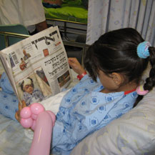 Hadeel Ma'ali, hospitalized in Israel after a settler threw a stone at her family near Yizhar, looks at her picture in the newspaper. Photo: Ronen Shimoni, B'Tselem, 5 Aug. '08.