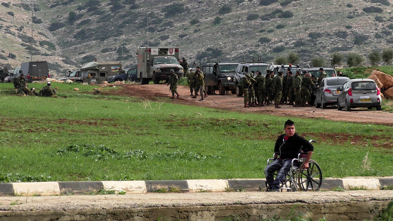 Palestinian passes by military forces training near al-'Aqabah. Photo by: ‘Aref Daraghmeh, 15 Feb. 2018