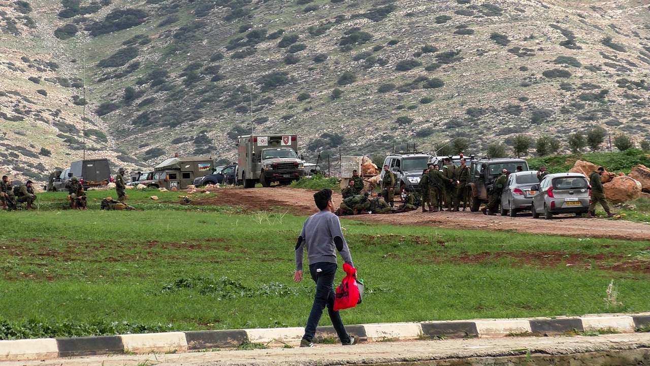 Palestinian passes by military forces training near al-'Aqabah. Photo by: ‘Aref Daraghmeh, 15 Feb. 2018