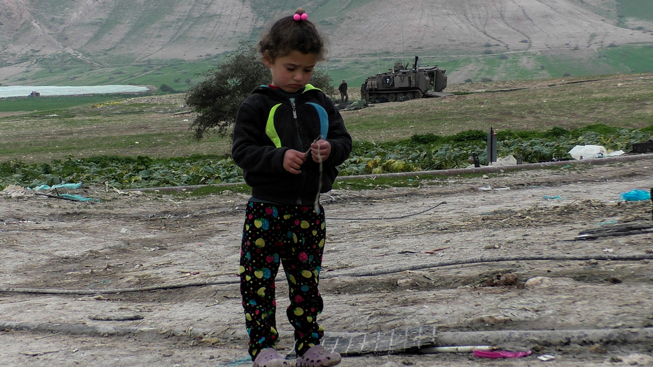 Palestinian girl with armored personnel carrier in background. Photo by: ‘Aref Daraghmeh, al-Farisiyah, 7 Feb. 2017