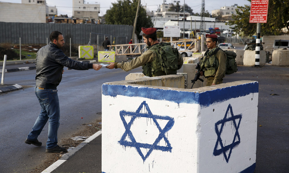 Soldiers inspect passersby at the entrance to village of Beit ‘Einun. Photo by Baz Ratner, Reuters, 1 December 2015