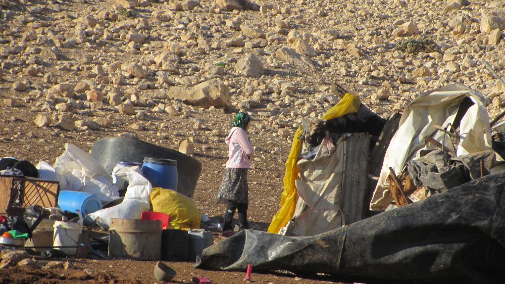 Resident of ‘Ein Karzaliyah against the background of the ruins of the community's buildings, 8.1.14
