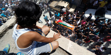 A Palestinian boy watches a funeral at Qalandiya Refugee Camp near the West Bank city of Ramallah August 26, 2013. Photo: Mohamad Torokman, Reuters.