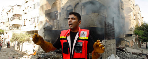 Member of emergency services crew in Gaza; background: house bombed on 10 July 2014. Photo: Ahmad Zakut, Reuters
