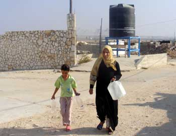 Resident of �Izbet �Abd Rabo in Jabalya refugee camp carrying home water from a container provided by OXFAM. Photo: Muhammad Sabah, B�Tselem, 18 Aug. �10