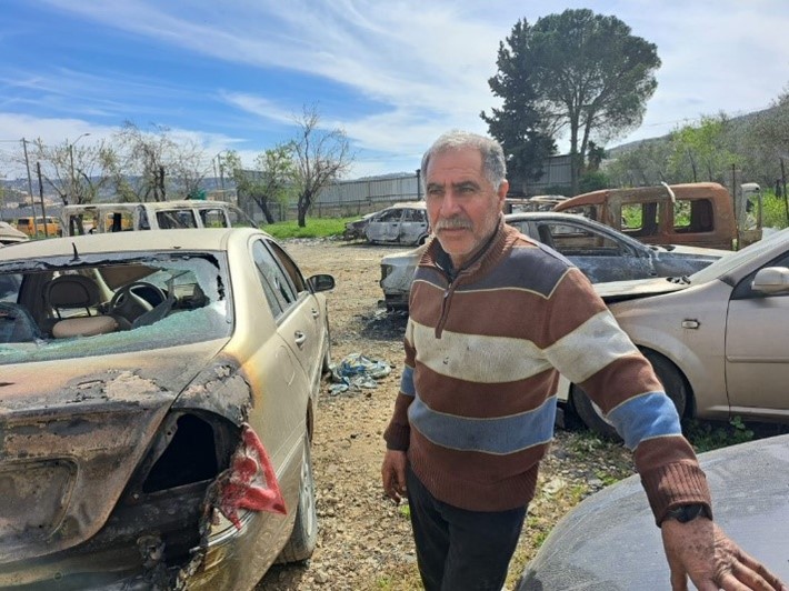 حسن عودة وخلفه سيّارات أحرقها المستوطنون. تصوير: عبد الكريم سعدي، بتسيلم 7.3.23 