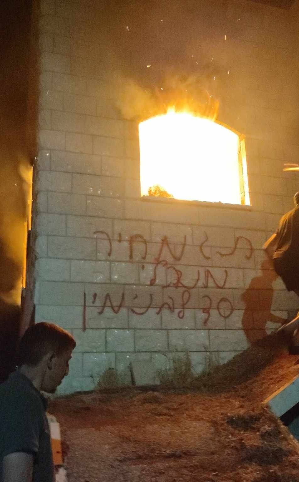 The Dawabsheh home, on fire, with the graffiti sprayed by the settlers. Photo courtesy of local residents 