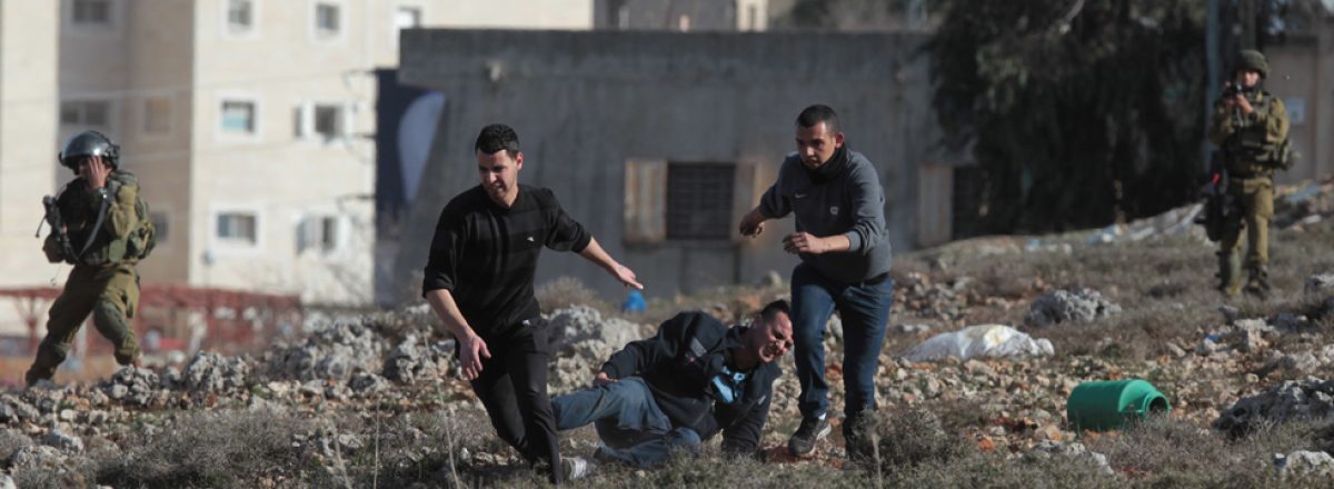 מפגין פלסטיני נופל על הקרקע לאחר שנפצע בעימות עם חיילים במחנה הפליטים ג'לזון. ברקע בתי ההתנחלות בית אל. צילום: עבאס מומאני, גטי אימג'ס, 31.1.14.