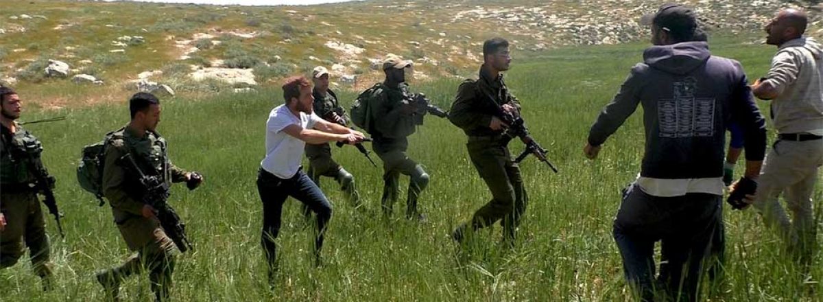 Still frame from video shot by B’Tselem volunteer Basel al-’Adrah: Armed Israeli settler accompanied by soldiers threatens Palestinian farmers near a-Tuwani, South Hebron Hills, 18 April 2020