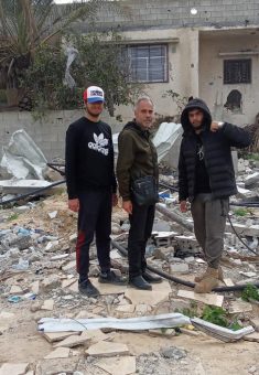 محمّد العجلة وابناه بجوار أنقاض مباني عائلة الرياطي التي تعرّضت للقصف في دير البلح. الصورة قدمتها العائلة مشكورة