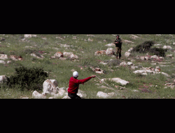 عاطف حنايشة يقف قبالة ضابط على التلّة حيث قُتل. تصوير نضال اشتيّة، وكالة أناضولو، 19.3.21