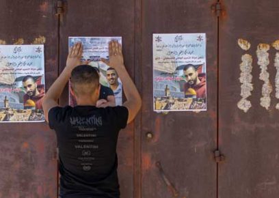 A youth hanging up posters with photos of the dead ahead of their funeral. Photo: Avishay Mohar, Activestills&nbsp;
