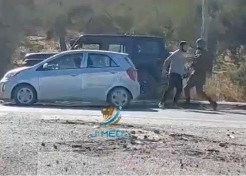 A soldier tries to prevent the settler from throwing stones at cars. Photo by Muhammad Fares