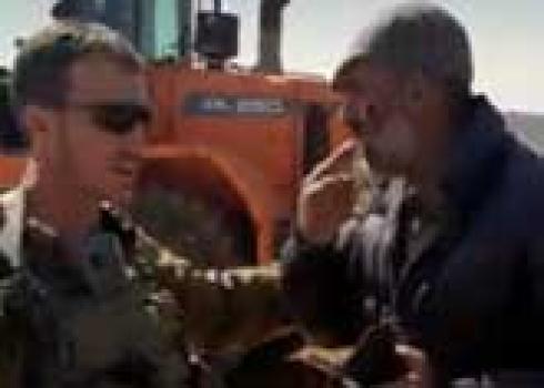 Ibrahim al-Mahariq pointing out the injury to his cheek to one of the soldiers. The settler-driven tractor is seen in the background. Photo courtesy of the al-Mahariq family 