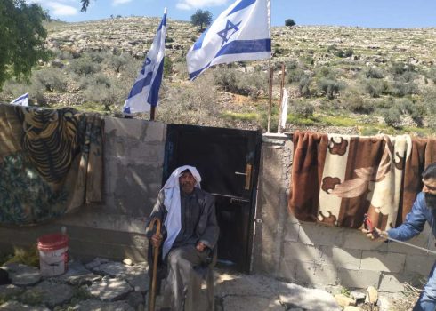 حمد العزازمة في باحة منزله. فوق رأسه أعلام نصبها المستوطنون على الجدار. تصوير:  سلمى الدبعي, بتسيلم، 25.4.25