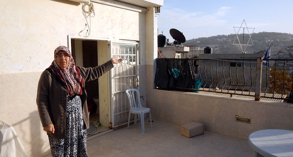  أم ناصر، من سكان الحيّ، والمستوطنة التي أقيمت بجوار منزلها. تصوير: حسام عابد، بتسيلم، 23.11.16 